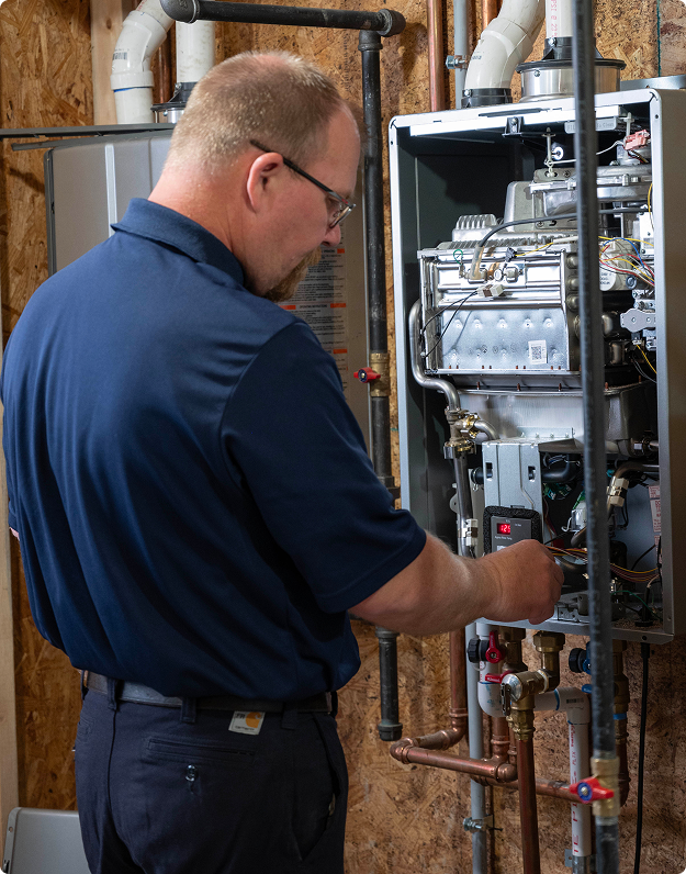 Hero technician in a navy uniform servicing an open boiler and copper supply piping in a basement mechanical room