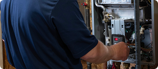 Close view of a technician's hands servicing an open boiler unit surrounded by copper piping