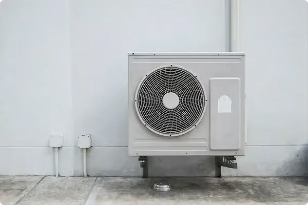 Outdoor heat pump condenser unit mounted on brackets against the exterior wall of a home