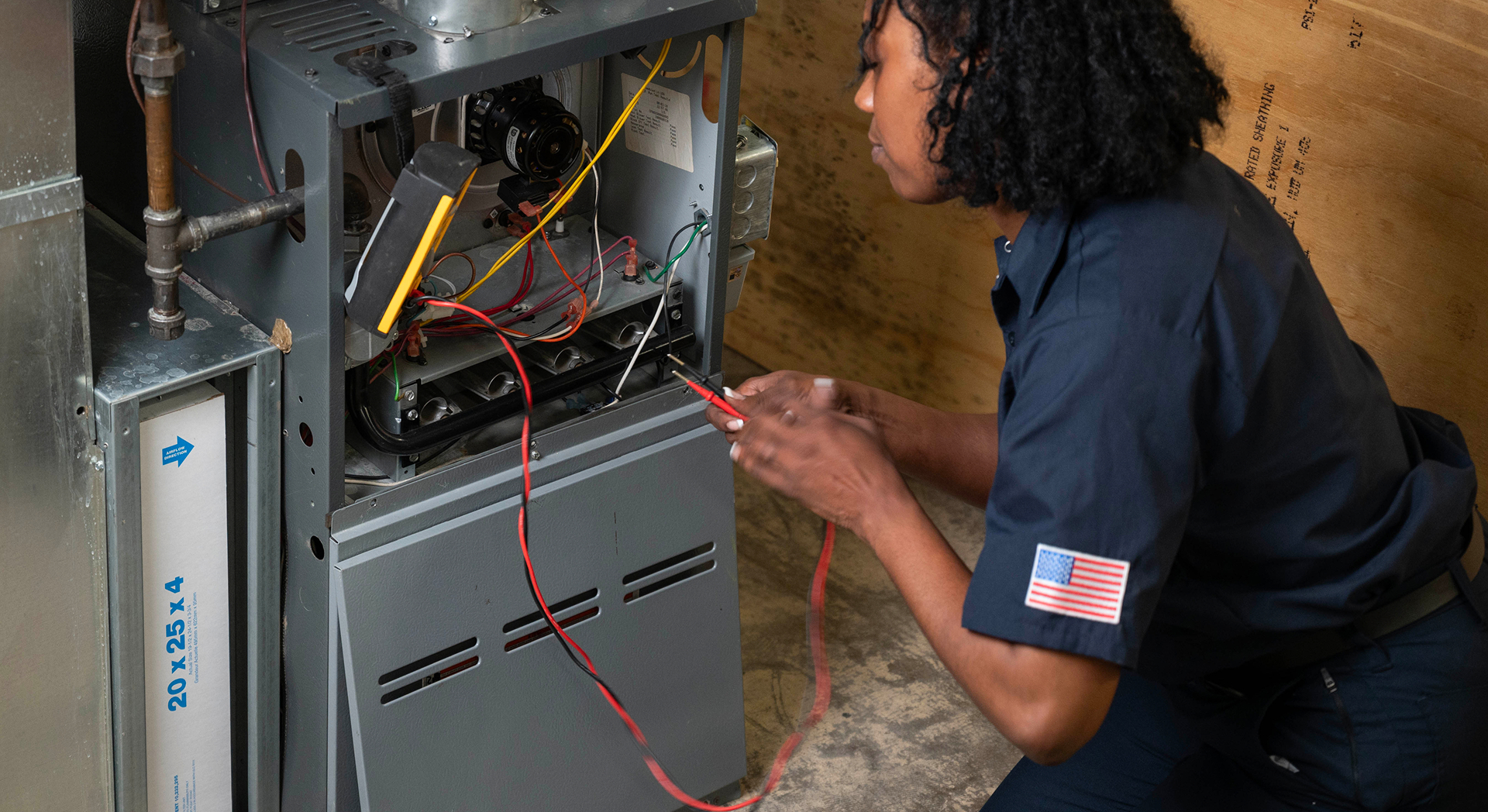 Technician using multimeter leads to test the controls inside an open furnace cabinet