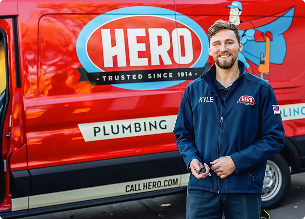 Hero Home Services technician standing beside a red Hero service van marked Plumbing, Heating and Cooling with the callhero.com web address