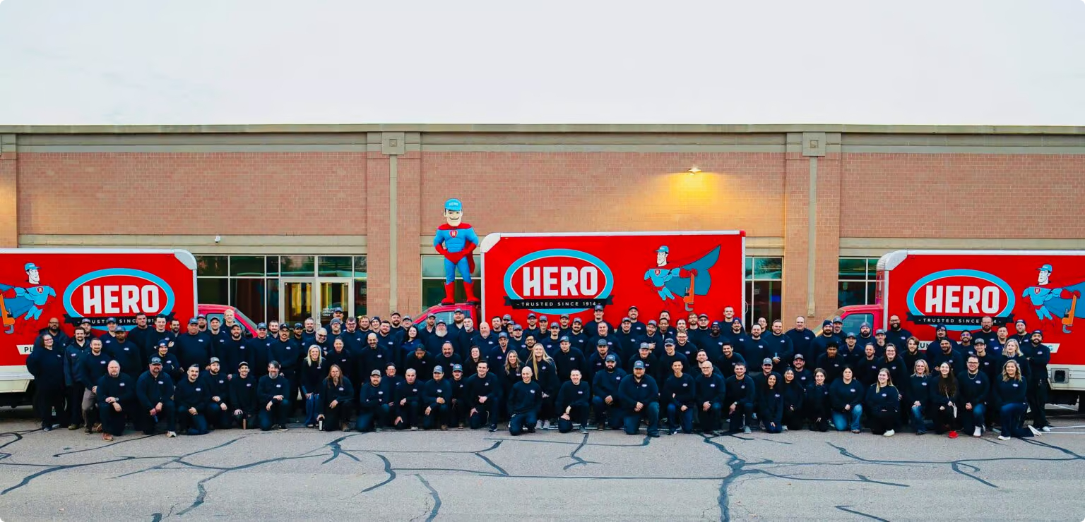 The full Hero Home Services team assembled outside the company building between large red Hero signs