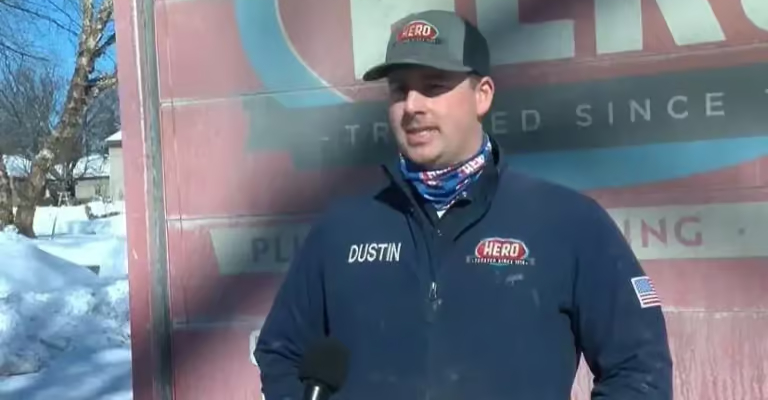Hero technician Dustin in a branded jacket and cap speaking to a news camera outside in the snow, with a Hero van behind him