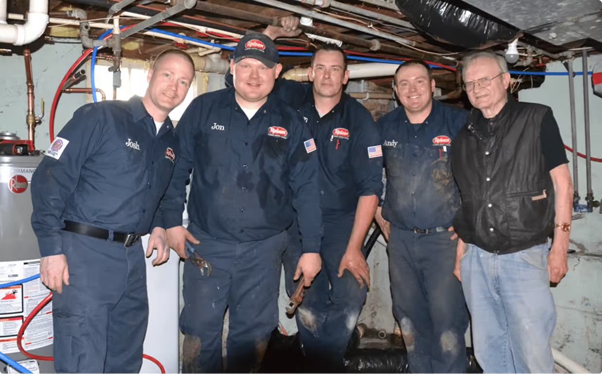 Five Hero Home Services employees standing together in a mechanical room lined with pipes and ductwork